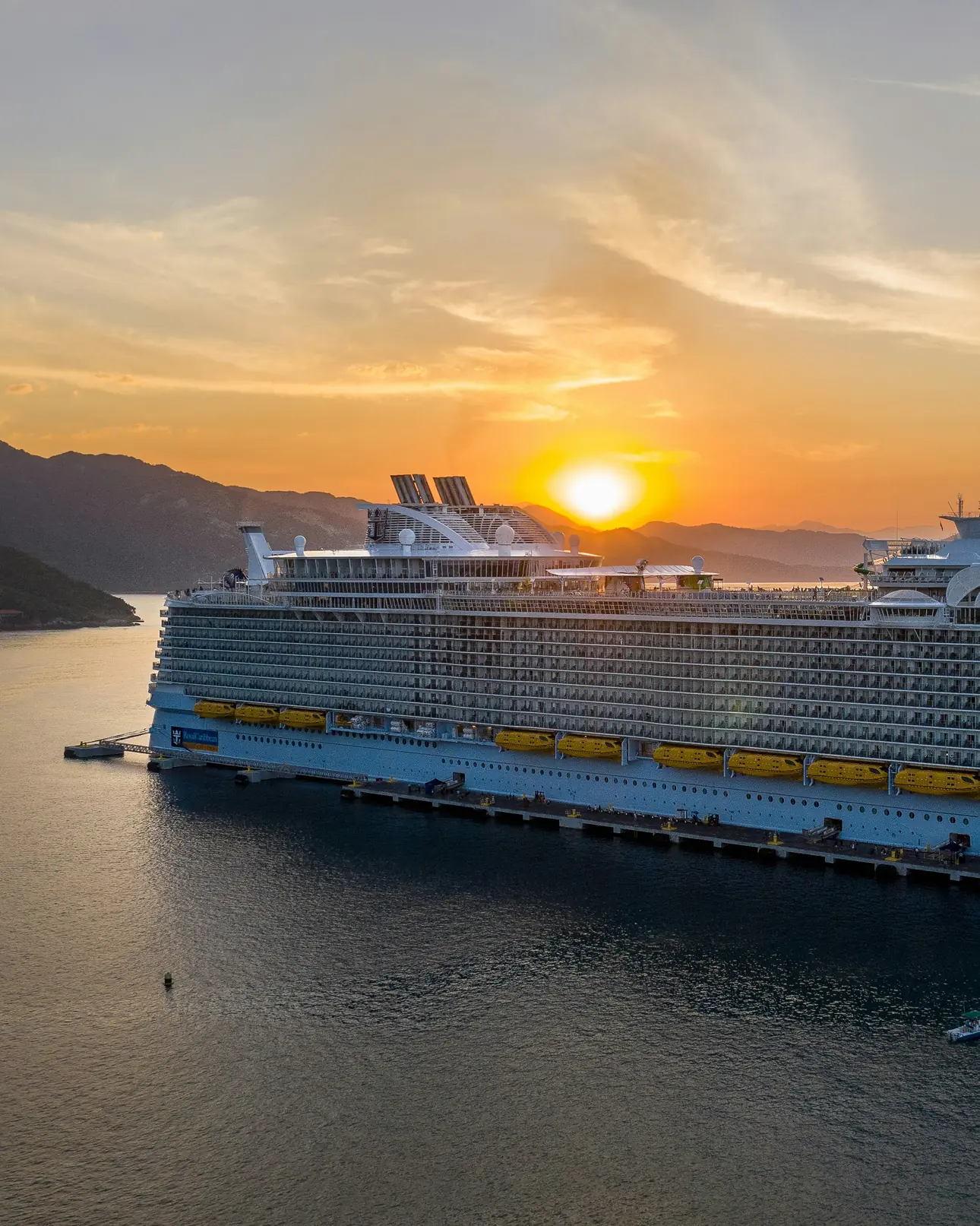 Nava Symphony of the Seas la apus, într-un golf cu munți.