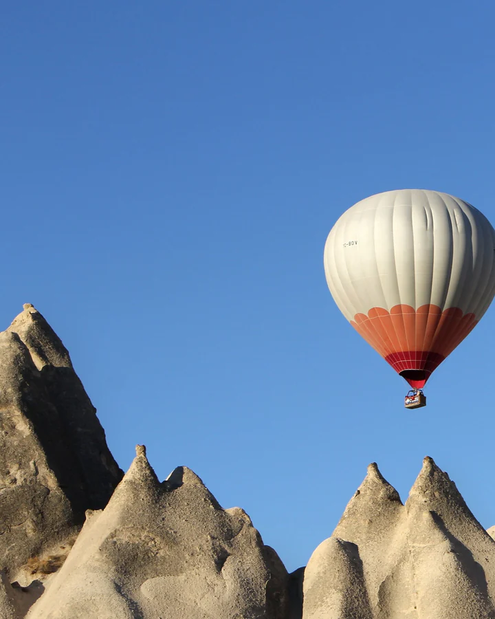 Baloane cu aer cald deasupra stâncilor din Cappadocia, pe cer albastru.