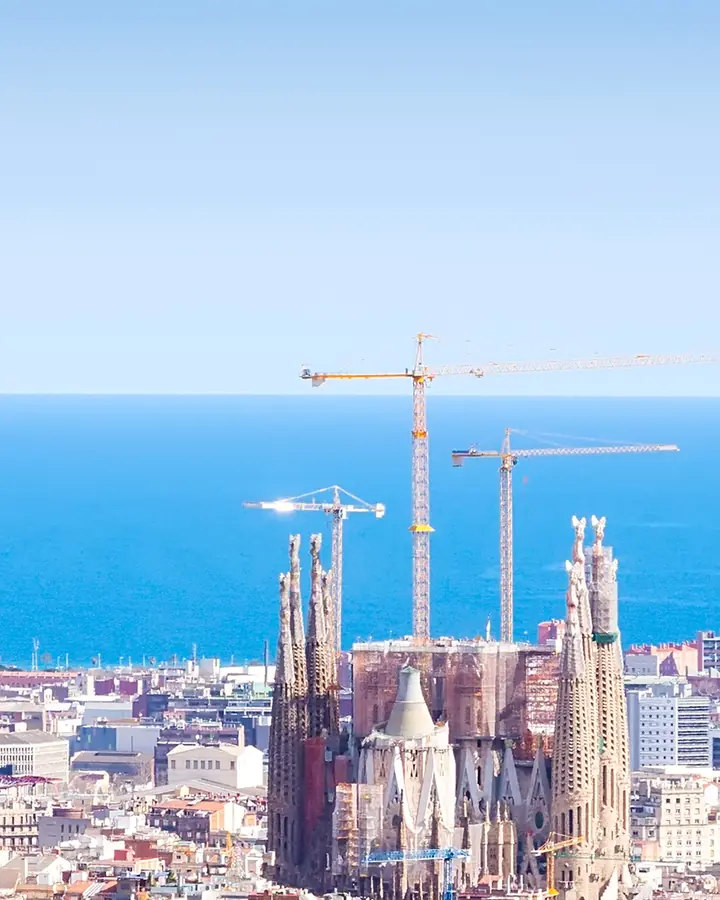 Sagrada Família, cu macaralele ei, deasupra acoperișurilor Barcelonei, cu marea în spate.